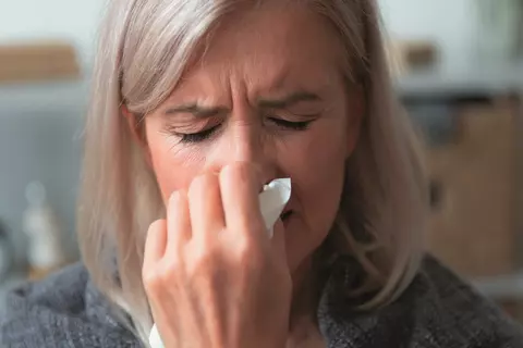 Žena si kýchla a drží si nos