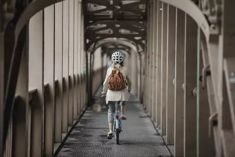Žena jede na kole, focena zezadu, má helmu a batoh