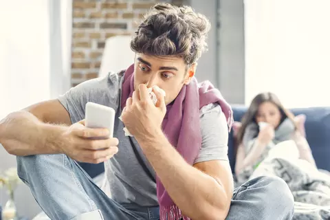 Muž smrká do kapesníku a kouká do mobilu, má kolem krku šálu